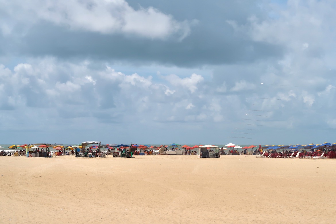 Dia nublado na praia de Atalaia, em Aracaju, com muitas pessoas na areia.