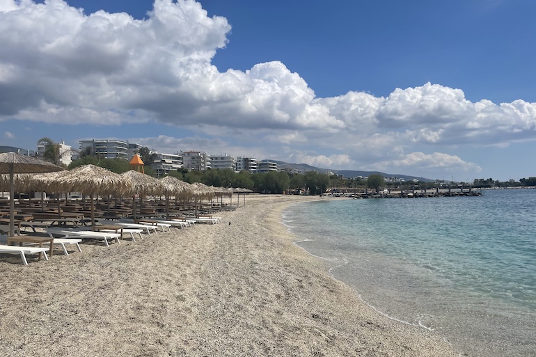 Praia de águas calmas e cristalinas na Riviera de Atenas, com bons hotéis na orla, inclusive alguns com vista para o mar.